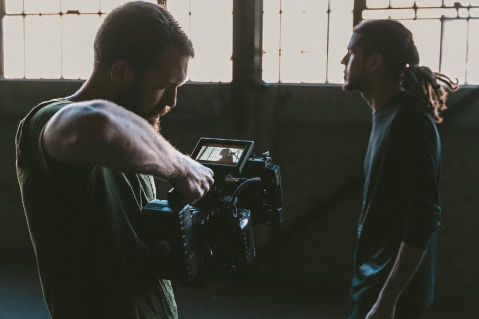 A camera operator filming a person on location in a sunlit warehouse.